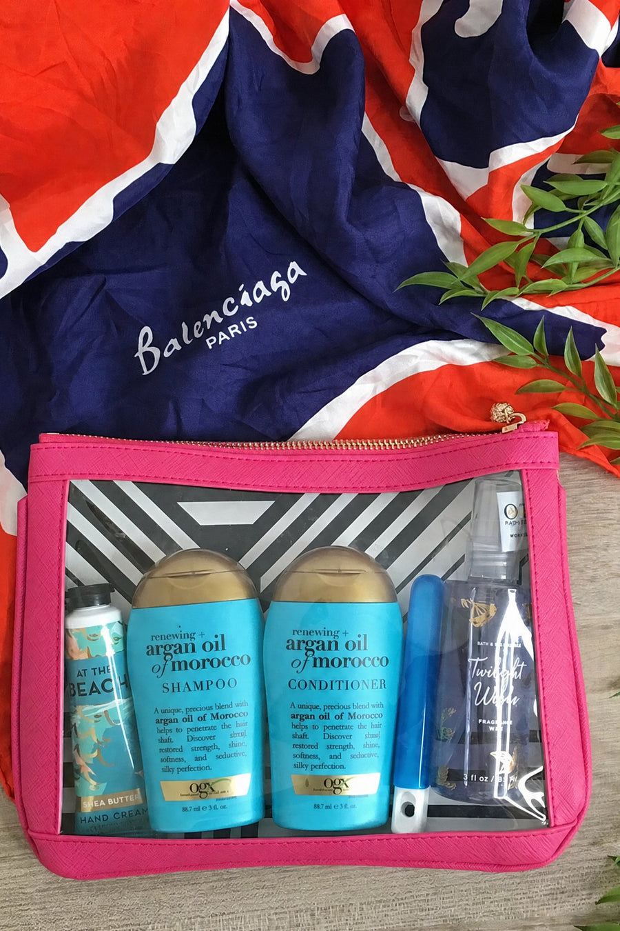 Hot pink #4 Nudie clear-window pouch packed with travel-size shampoo, conditioner and sunscreen, styled on a silk scarf
