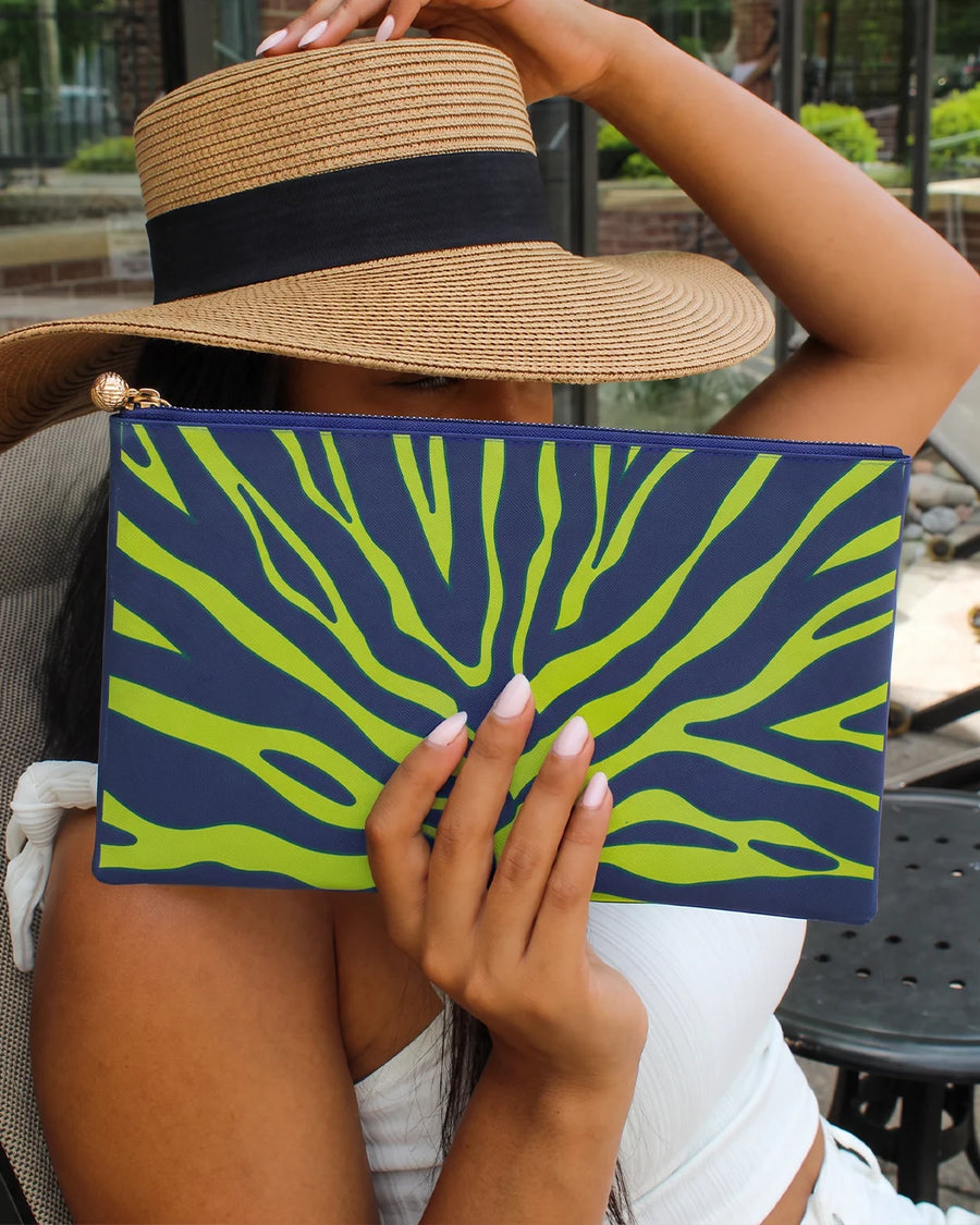 Woman in a straw sun hat holding the OTG #5 Leighton navy and green print clutch