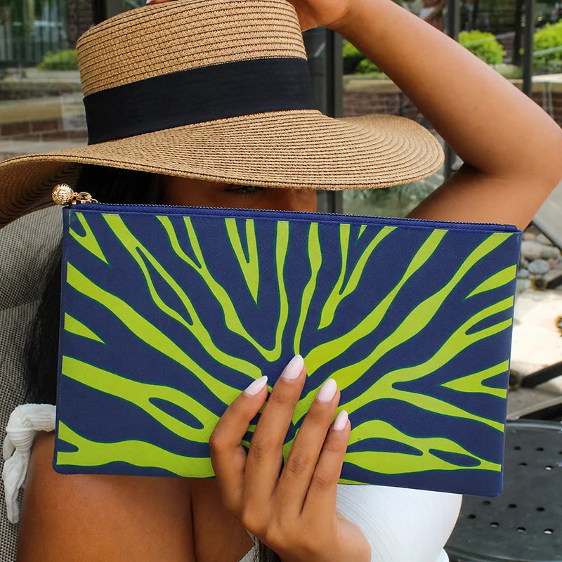 Person holding a blue and green patterned clutch with a straw hat.