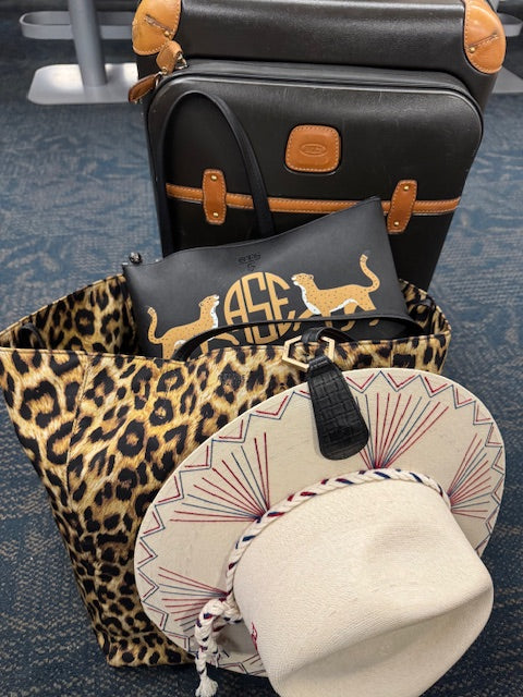 Black #5 size OTG247 bag peeking out of a leapord print carry bag next to luggage.
