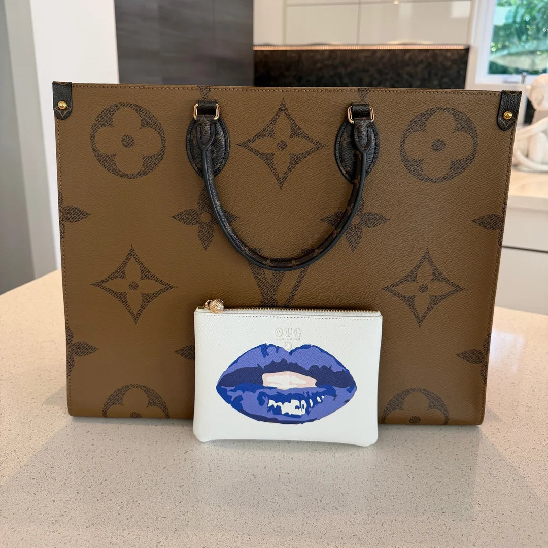 White #2 pouch with blue lips print in front of a monogram tote