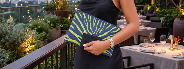 Person holding a green and blue clutch with a pattern, next to a table setting with plates and glasses.