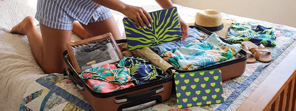 Person packing a suitcase with tropical-themed clothing on a bed.